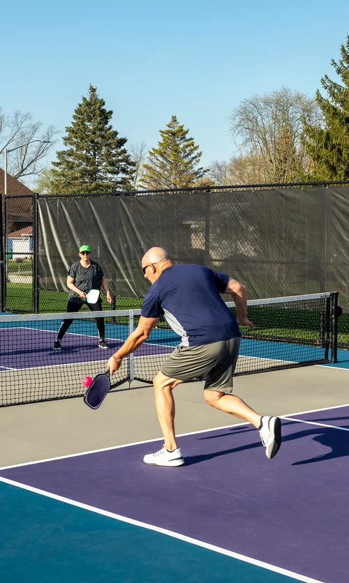 Four adults playing pickleball on an outdoor court with colorful blue and purple surfaces.