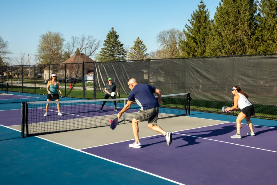 Four adults playing pickleball on an outdoor court with colorful blue and purple surfaces.