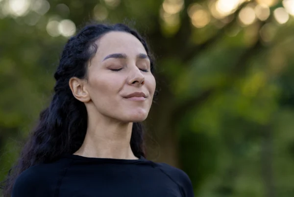 Woman standing outdoors with eyes closed, practicing calm, controlled breathing with relaxed posture