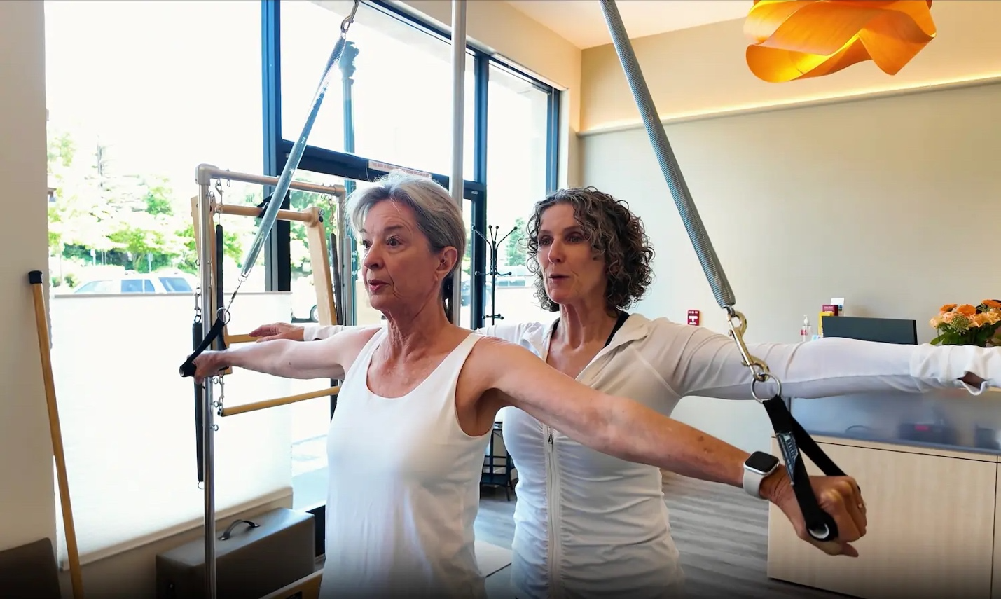 Kathleen McDonough guiding a patient through a Pilates exercise using resistance equipment.